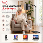 Heedy floor tablet stand beside an older woman in an armchair, showing hands-free tablet use, adjustable positioning and 360-degree rotation.